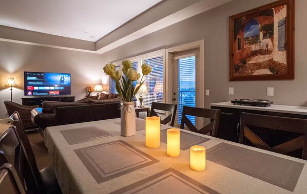 Un salon avec un téléviseur, un canapé, une table à manger décorée de bougies et un tableau accroché au mur.