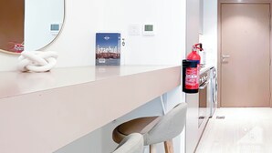 Une chambre d’hôtel avec un comptoir blanc, un extincteur, un miroir, une chaise et une porte.
