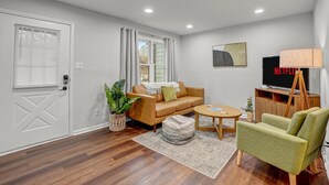 Un salon moderne avec un canapé, un fauteuil et un téléviseur posé sur un meuble.