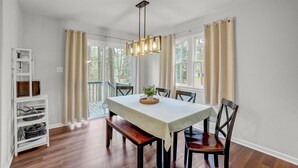 Un coin repas avec une table dressée pour quatre personnes, un luminaire suspendu et une vue sur l’extérieur grâce à de grandes fenêtres.