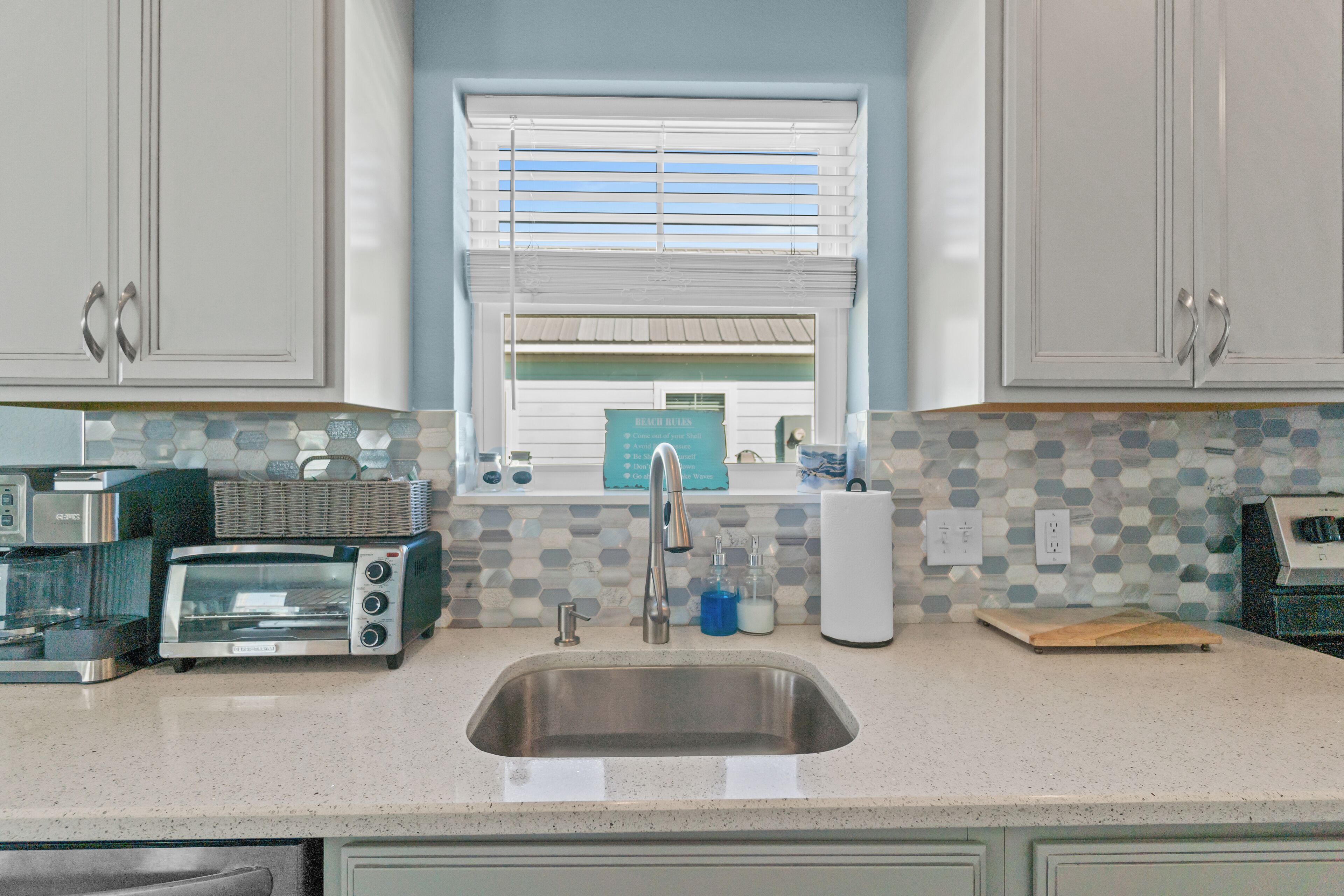 A kitchen with white cabinets, a stainless steel sink, a toaster, and a window with blinds.