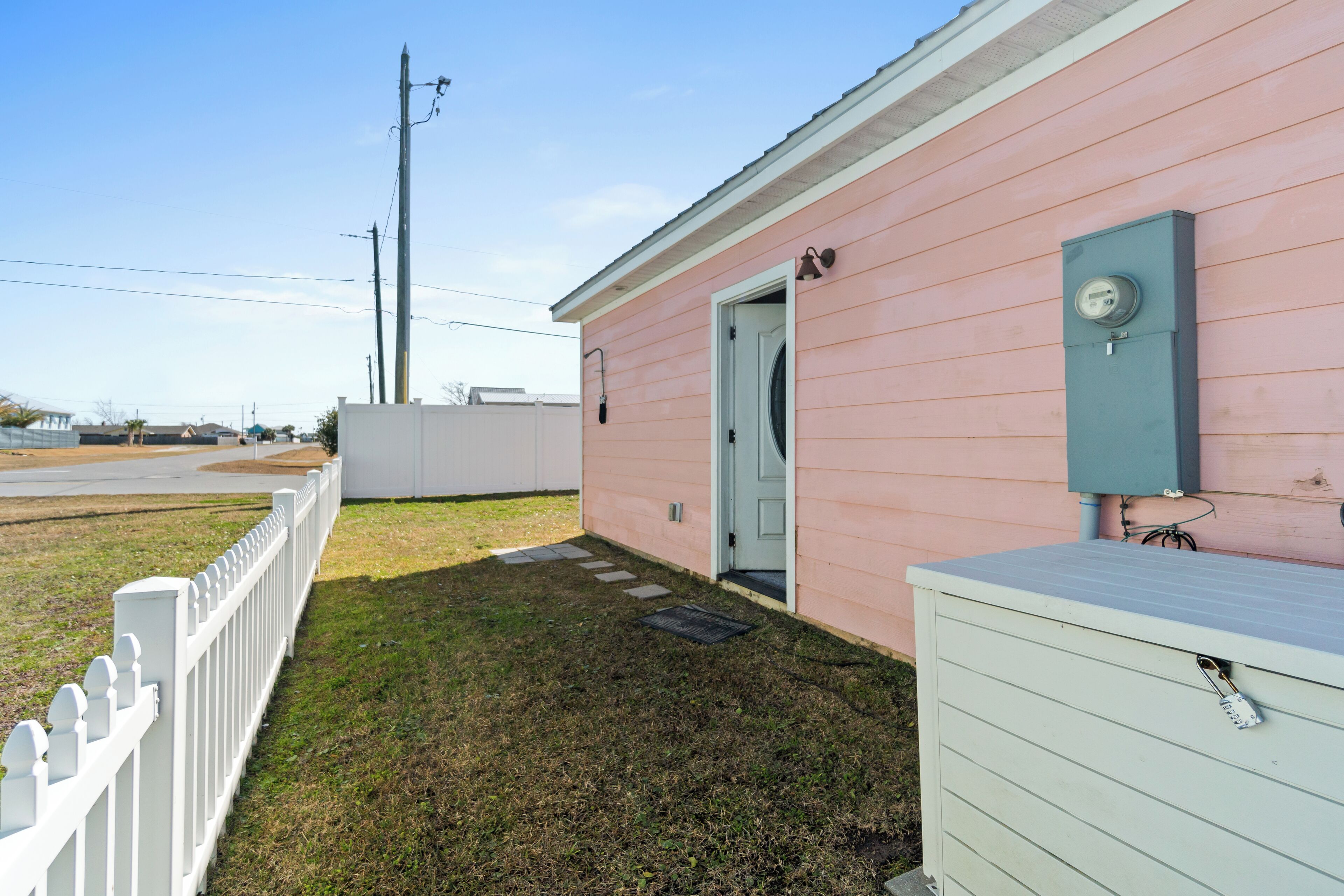Charming pink coastal cottage with white picket fence and storage chest in a peaceful neighborhood setting.