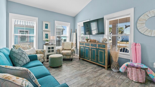 A living room with a blue sofa, a patterned armchair, a wooden cabinet, and a television on the wall.