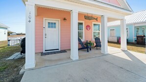 A pink house with a white porch, number 104, and a sign that says "Beach House".