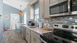 A kitchen with a stainless steel refrigerator, a microwave, and a stove. There is a window with blinds, a sink, and a chair.