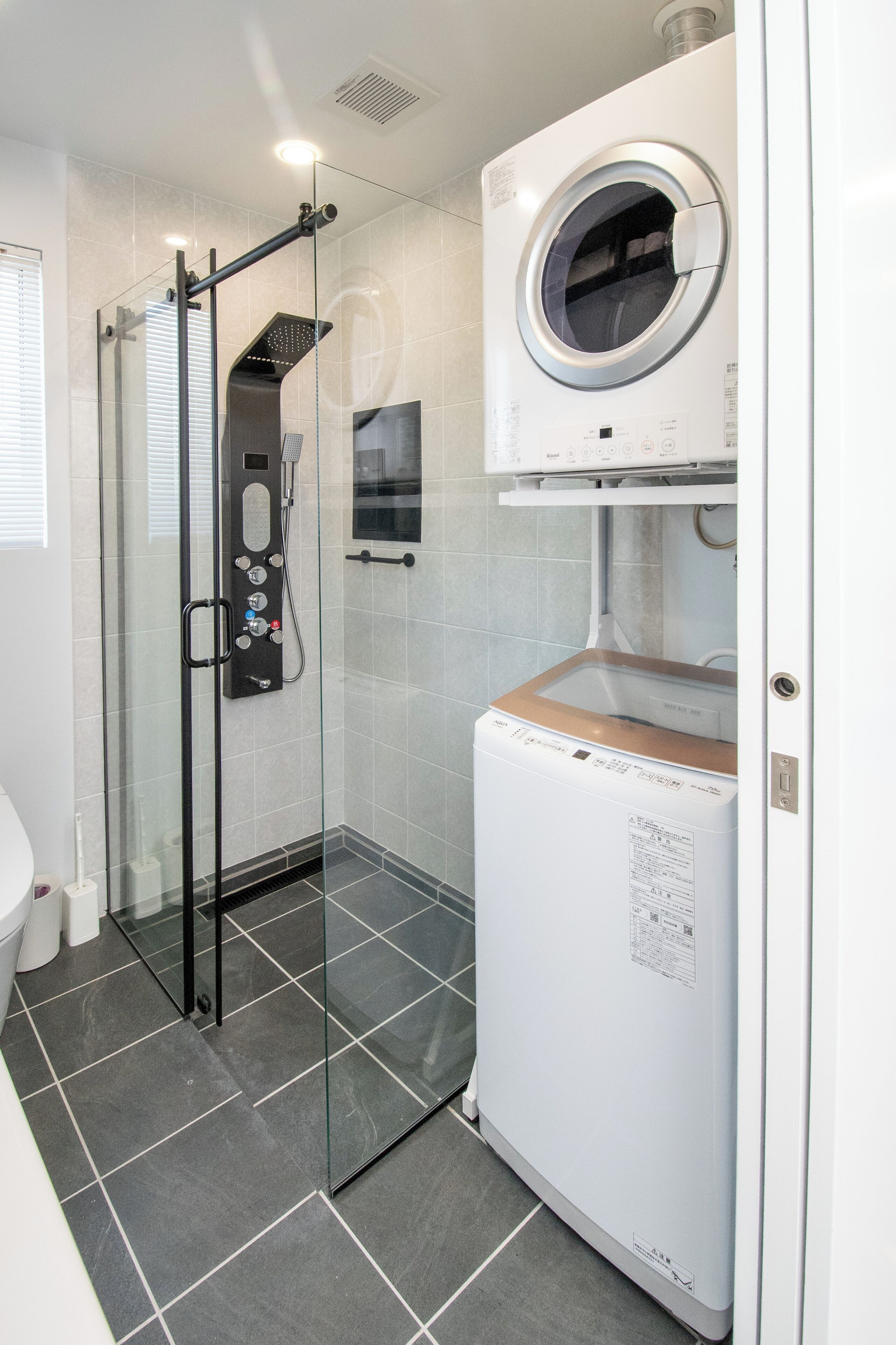A compact bathroom with a glass-enclosed shower, a built-in washing machine, and a toilet.