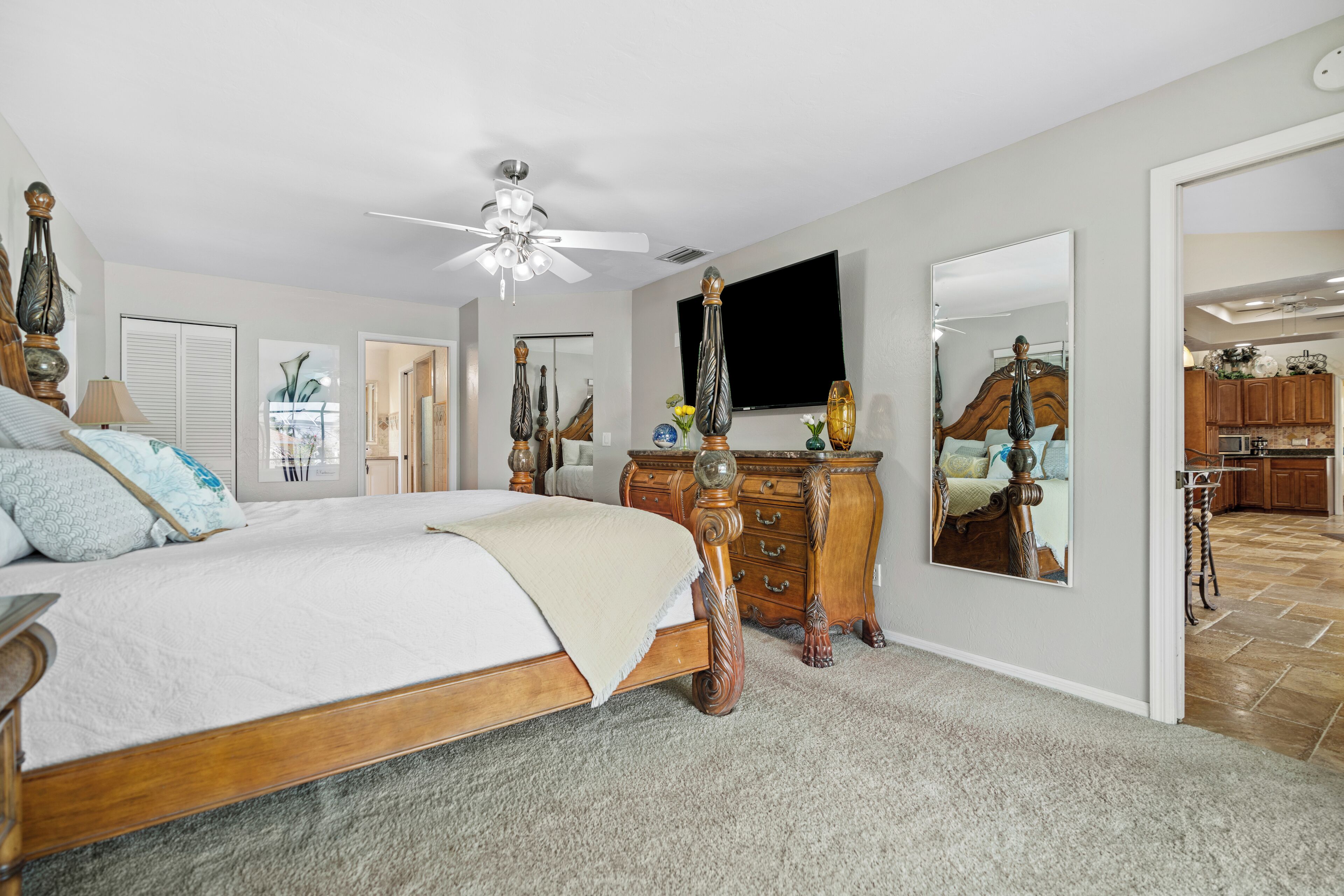 A bedroom with a large bed, a dresser, a mirror, and a ceiling fan.