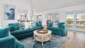 A spacious living room with teal sofas, a round coffee table, and a ceiling fan. - Waterfront Home w/ Private Pool | Key Allegro | 5BR · Sleeps 14 (Rockport)