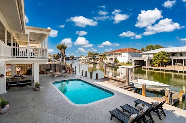 A pool area with lounge chairs, a dock, and a view of a marina.