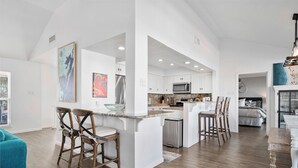 A spacious kitchen with white cabinetry, a central island with bar stools, and a dining area with a table and chairs. - Waterfront Home w/ Private Pool | Key Allegro | 5BR · Sleeps 14 (Rockport)