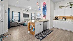 A modern kitchen with white cabinets, a wooden island, and a large surfboard decoration. - Coastal Getaway w/ Community Pool + Fishing Nearby (Rockport)