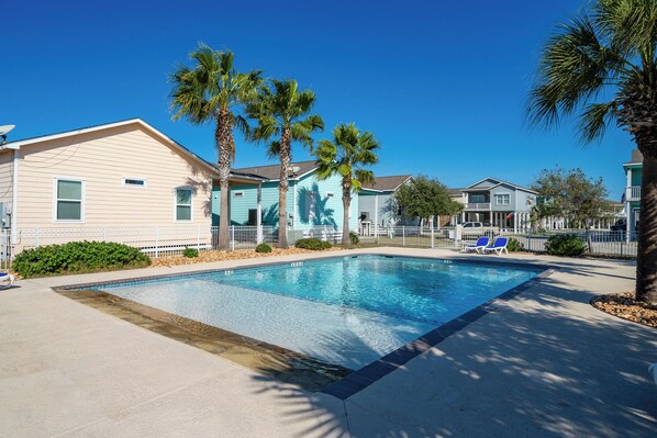 Piscina rodeada de casas, con palmeras y una valla.