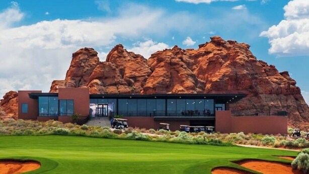 A modern building with a glass facade, situated in a desert landscape with red rock formations in the background. - Grand Gathering Retreat-Private Heated Pool-Mini Golf-Sand Hollow ATV Mecca-Zion (Hurricane)
