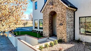 A modern house with a stone archway entrance, a well-maintained lawn, and a clear sky. - Grand Gathering Retreat-Private Heated Pool-Mini Golf-Sand Hollow ATV Mecca-Zion (Hurricane)