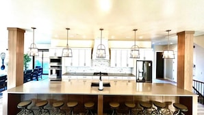 A modern kitchen with a central island, bar stools, stainless steel appliances, and pendant lighting. - Grand Gathering Retreat-Private Heated Pool-Mini Golf-Sand Hollow ATV Mecca-Zion (Hurricane)