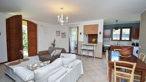 A living room with a sofa, a dining table with chairs, a kitchen area, and a large wooden door. - Villa Carini Holiday House by the Sea and Jacuzzi pool (Carini)