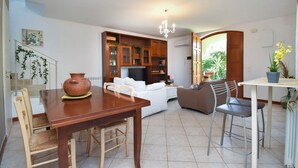 A spacious living area with a wooden dining table, white sofa, and a TV. There's a kitchen area with cabinets and a chandelier. - Villa Carini Holiday House by the Sea and Jacuzzi pool (Carini)