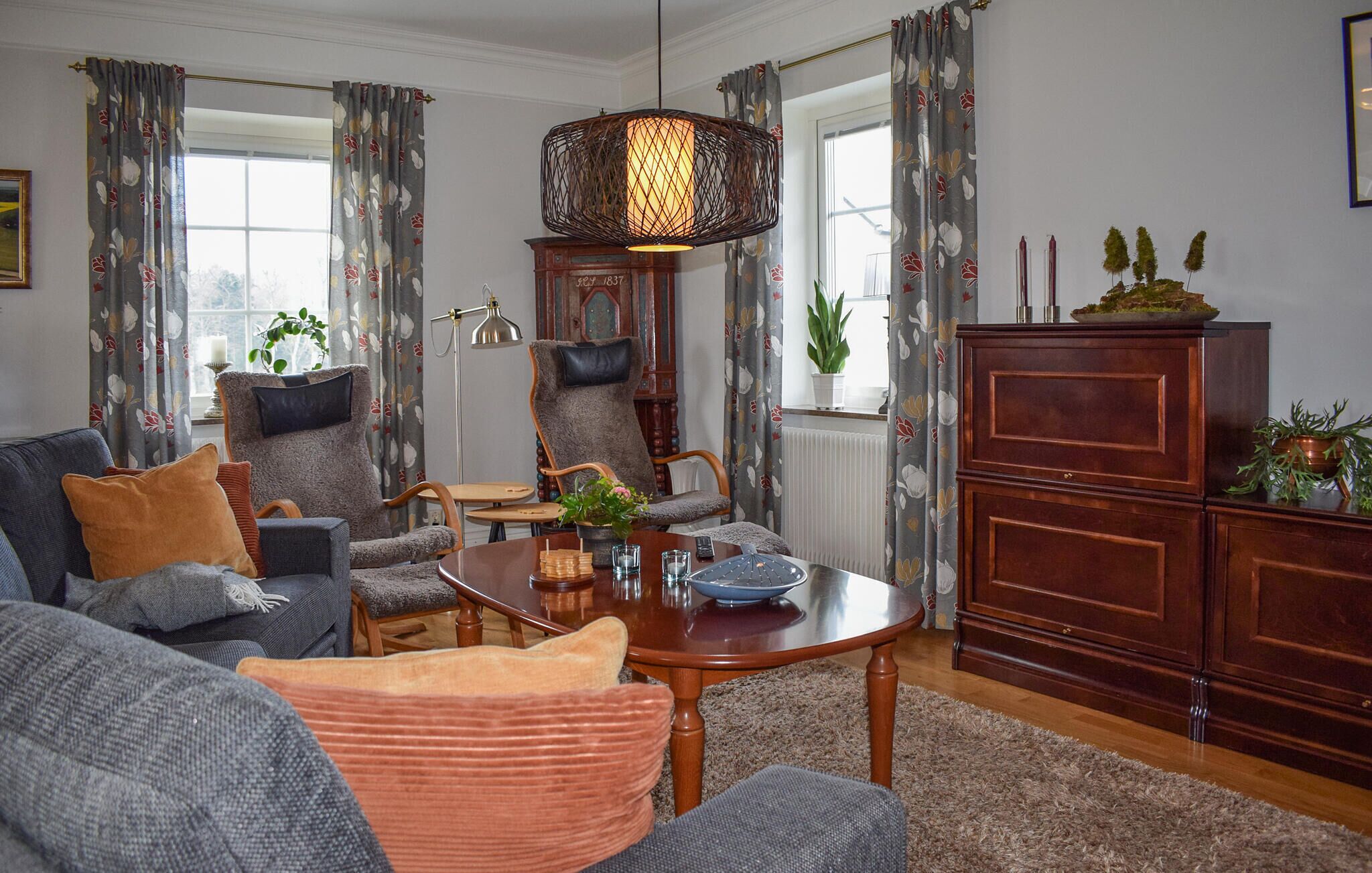 Ein gemütliches Wohnzimmer mit einer Couch, Sesseln, einem Holztisch und einer Vintage-Uhr.