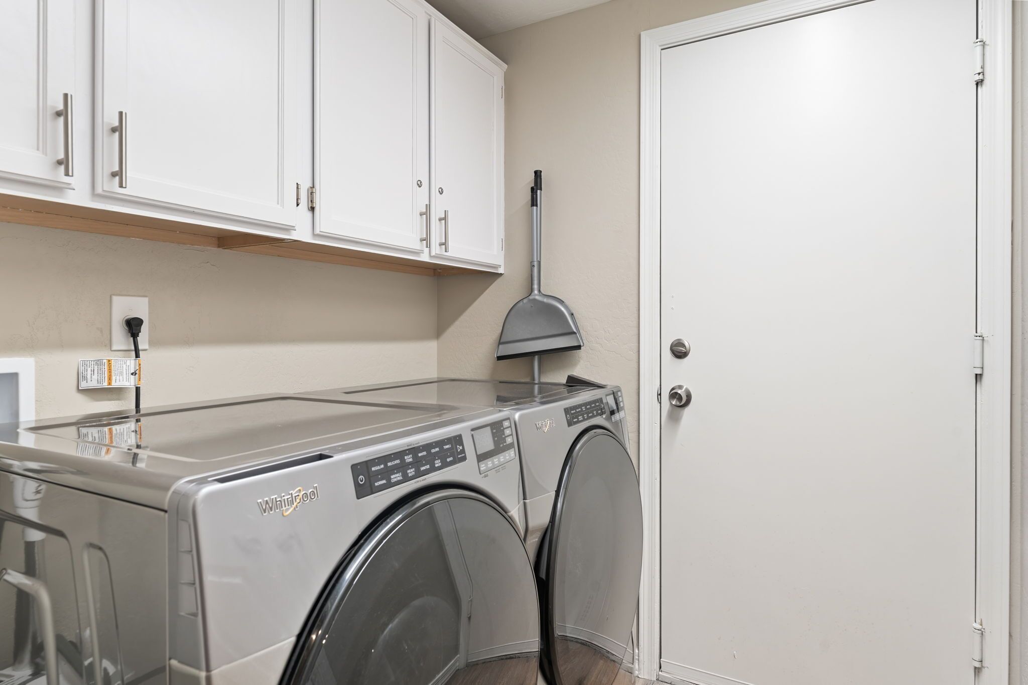 Un espace buanderie équipé d’un lave-linge et d’un sèche-linge Whirlpool, de meubles blancs et d’une porte.