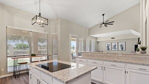 Una cocina amplia con armarios blancos, una isla con encimera de granito y un ventilador de techo.