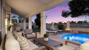 Un patio al aire libre con piscina, mobiliario y una parrilla.