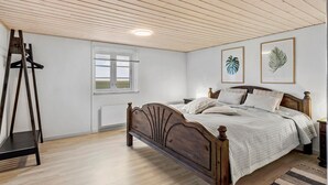 Een slaapkamer met een houten bed, een raam met jaloezieën, een radiator, en twee wanddecoraties met bladmotieven.