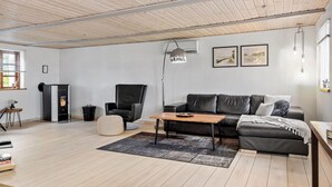 Een moderne woonkamer met een houten plafond, een leren zwarte bank, een houten salontafel en een open haard.
