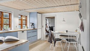 Een moderne keuken met houten balken, een eetgedeelte met witte stoelen en uitzicht op de omgeving.