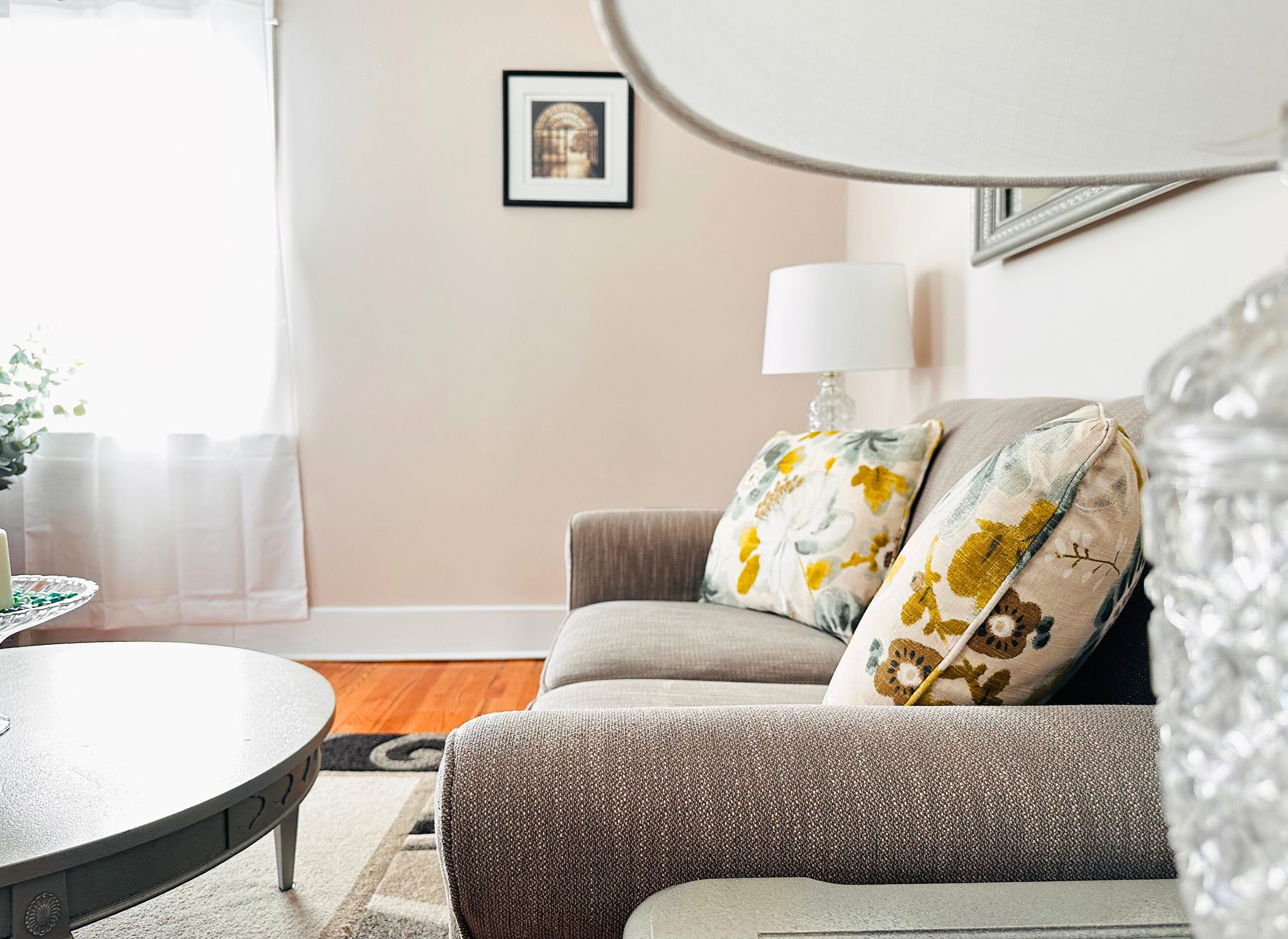 Ein Wohnzimmer mit einer Couch, zwei Kissen, einer Lampe und einem gerahmten Bild an der Wand.
