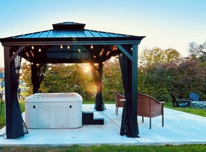 A gazebo with a hot tub, seating area, and string lights.