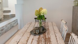 Una mesa de comedor rústica con un candelabro antiguo, sillas blancas y una escalera al fondo.