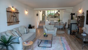 Un amplio salón con sofá, mesa de centro y una mesa de comedor con sillas. Se ve una escalera que sube a un nivel superior.