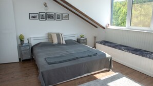 Un dormitorio con cama, mesita de noche, ventana y estante fijado a la pared.