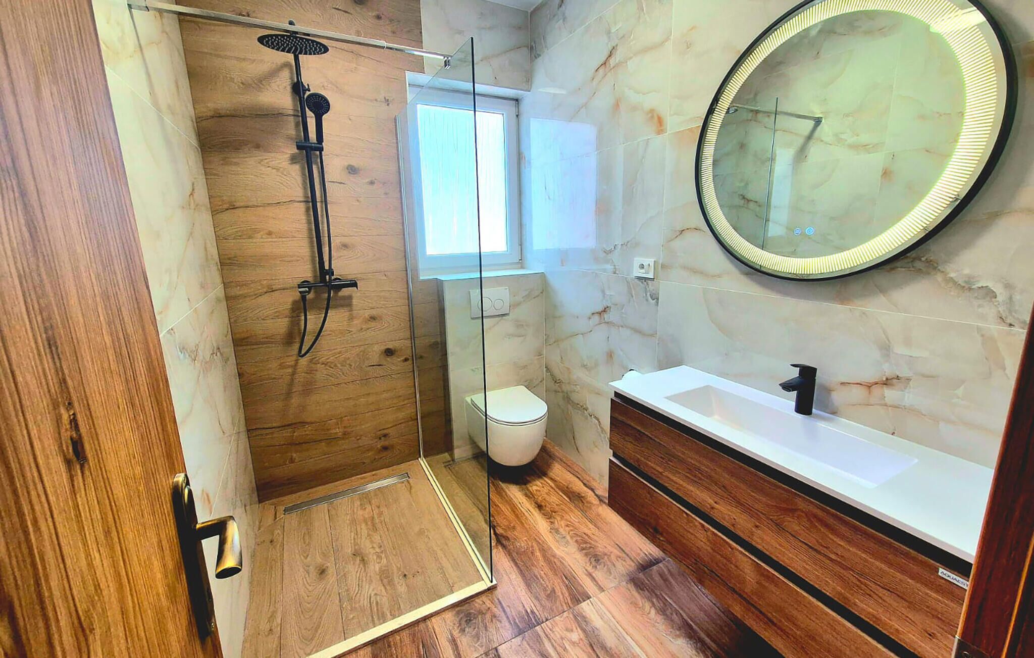 Een moderne badkamer met een douche met glazen wand, een wit toilet en een witte wastafel met een zwarte kraan.