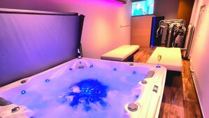 Ein Spa-Raum mit Whirlpool, Massageliege und Fernseher im Hintergrund.