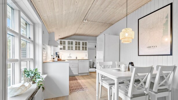 A modern kitchen with white cabinetry, a dining area with white chairs, and a large window with plants.