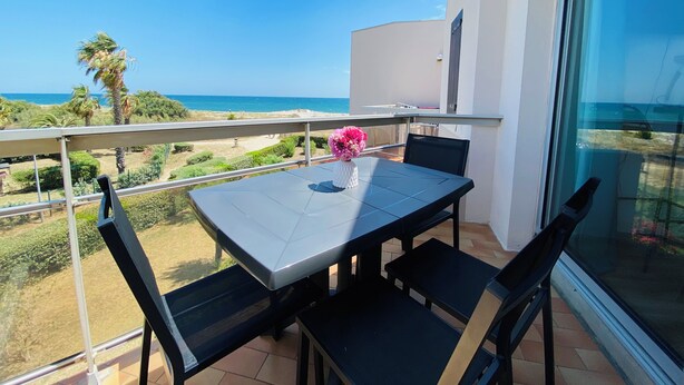 A balcony with a table and chairs, overlooking a beach and ocean.