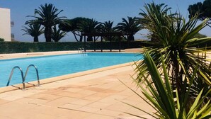 A swimming pool with a clear blue sky, palm trees, and a modern building in the background.
