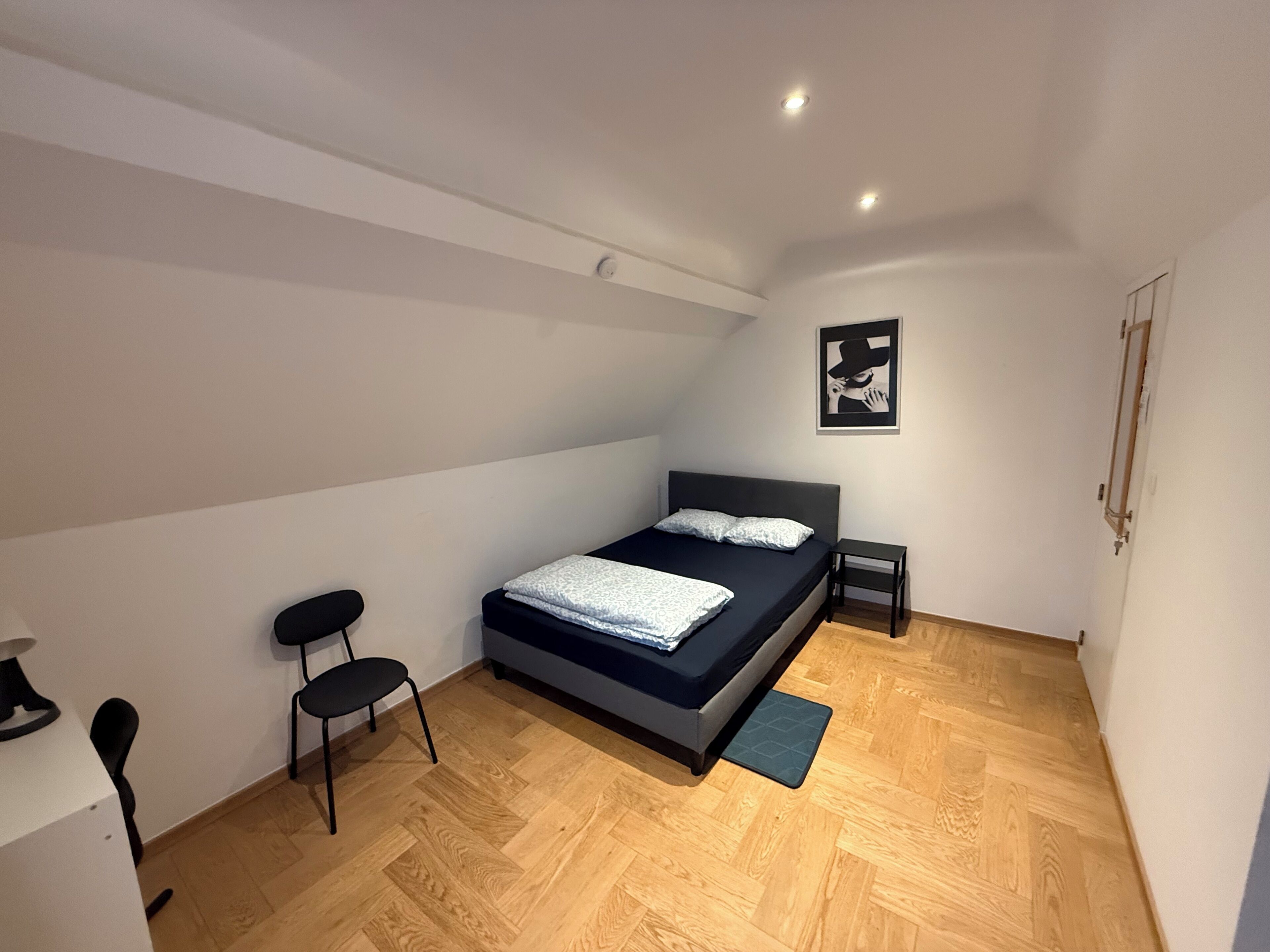 A modern bedroom with a bed, a chair, a small table, and a picture on the wall.