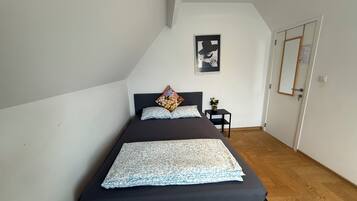 Quarto com cama, uma pequena mesa de cabeceira, um quadro na parede e uma porta com espelho.