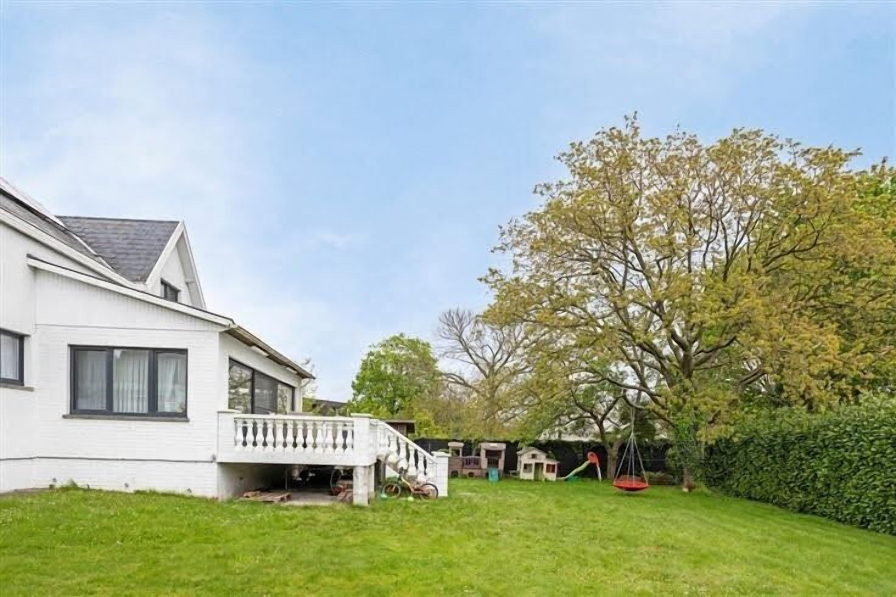 Une maison blanche avec un balcon, une balançoire et une pelouse bien entretenue.