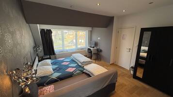 Et soveværelse med seng, skrivebord og computer. Der er et vindue med udsigt til huse.