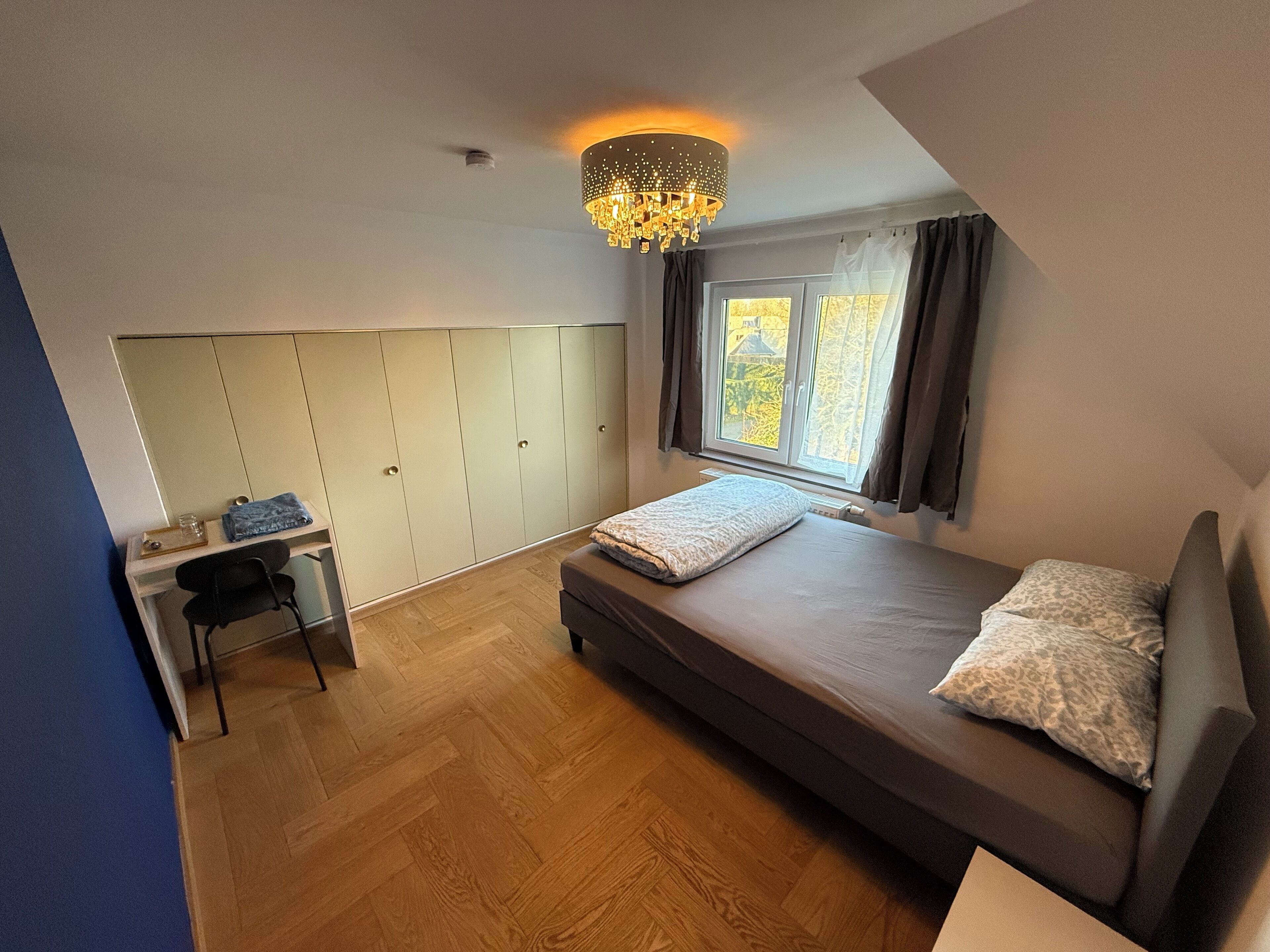 A bedroom with a bed, a desk, and a wardrobe.