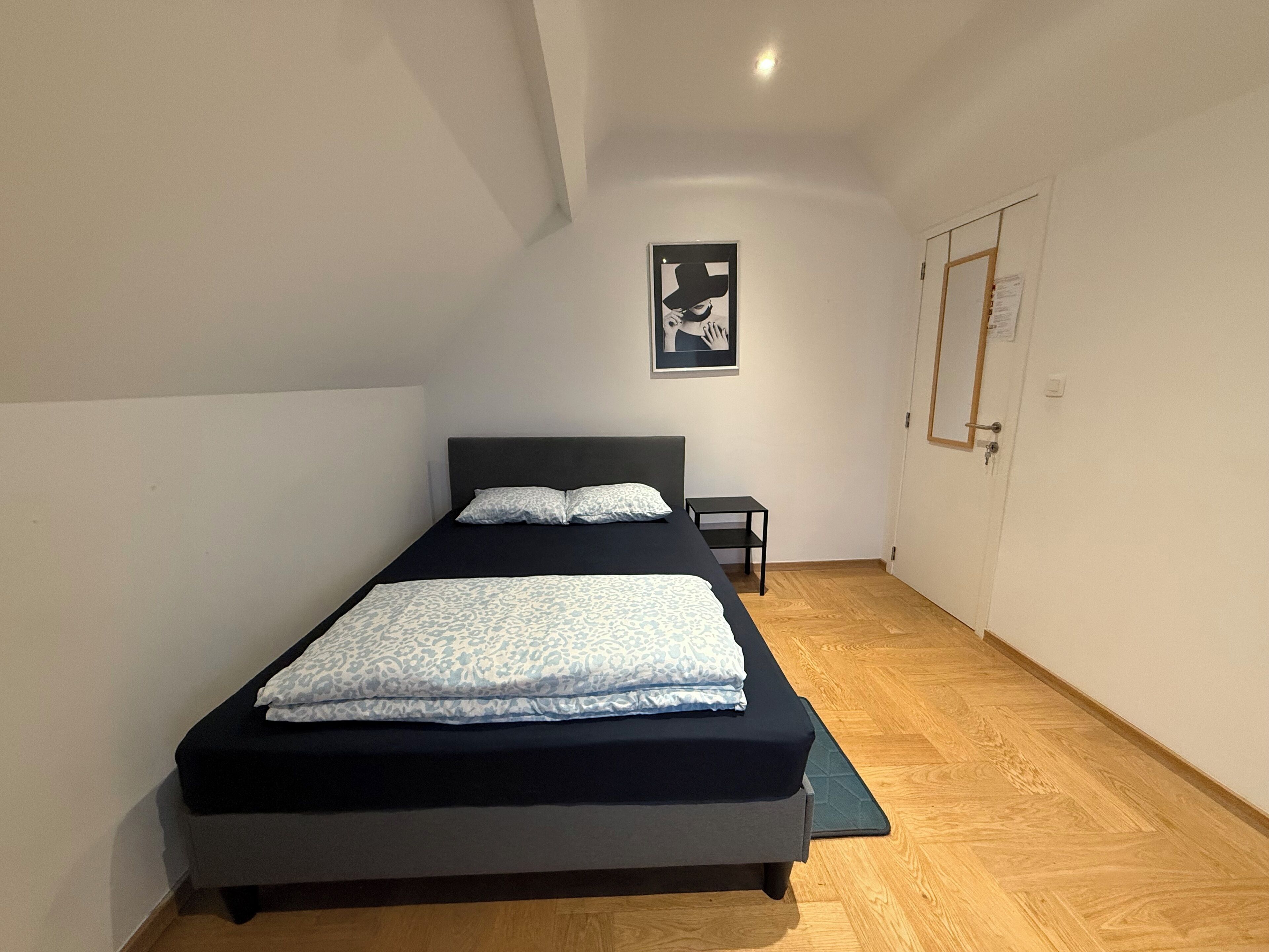 Une chambre à coucher avec un lit, une petite table de chevet et une affiche accrochée au mur.