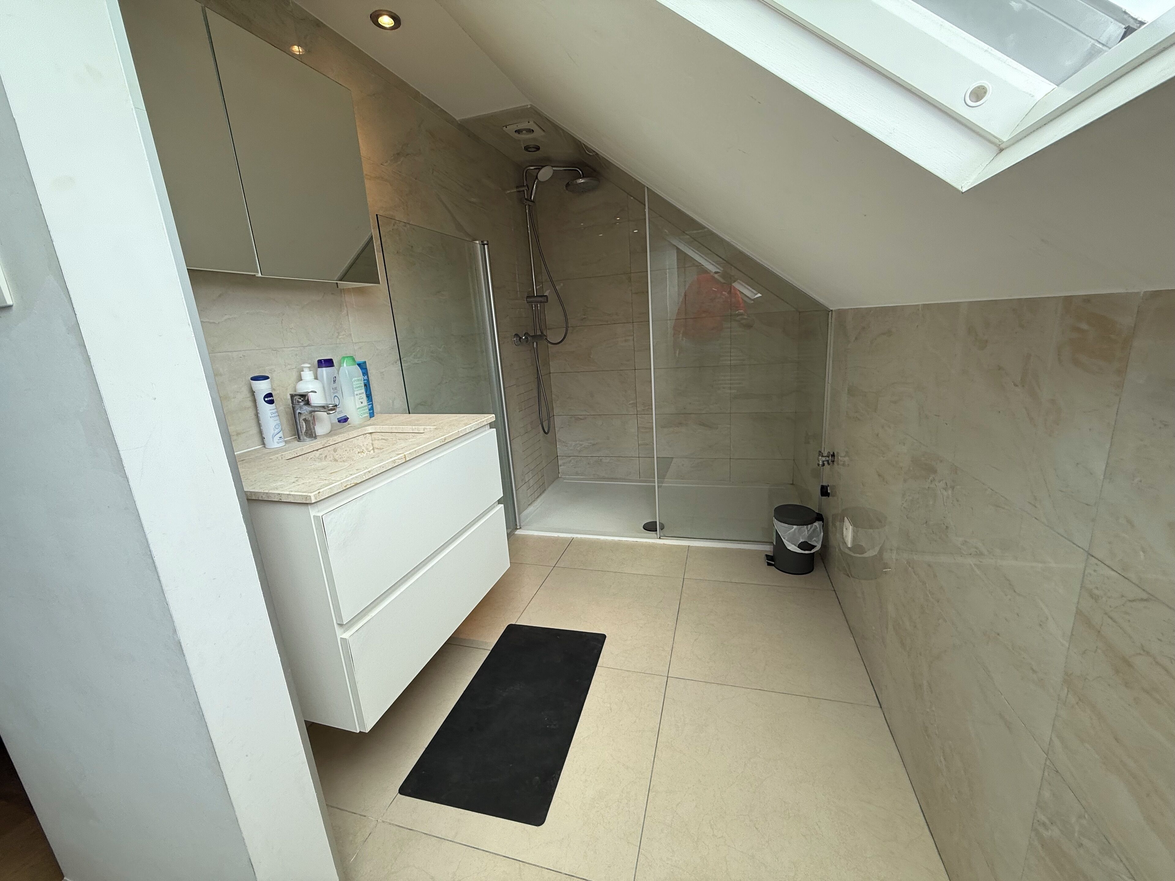 A modern bathroom with a glass shower enclosure, a white vanity, and a black bath mat.
