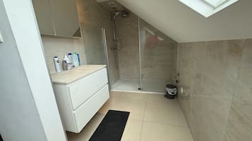 A modern bathroom with a glass shower enclosure, a white vanity, and a black bath mat.
