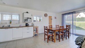 Une cuisine moderne avec des meubles blancs, une table à manger en bois et des chaises. Une fenêtre offre une vue sur l’extérieur.