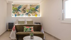 Een slaapkamer met een bed, een bank, een klein tafeltje en een muur met een wanddecoratie van tropische planten.