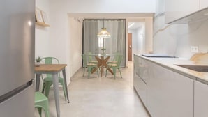 Een moderne keuken met witte kastjes, een eethoek met een ronde tafel en stoelen, en een hanglamp.