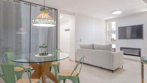 Een moderne woonkamer met een glazen eettafel, groene stoelen, een witte bank en een open haard.